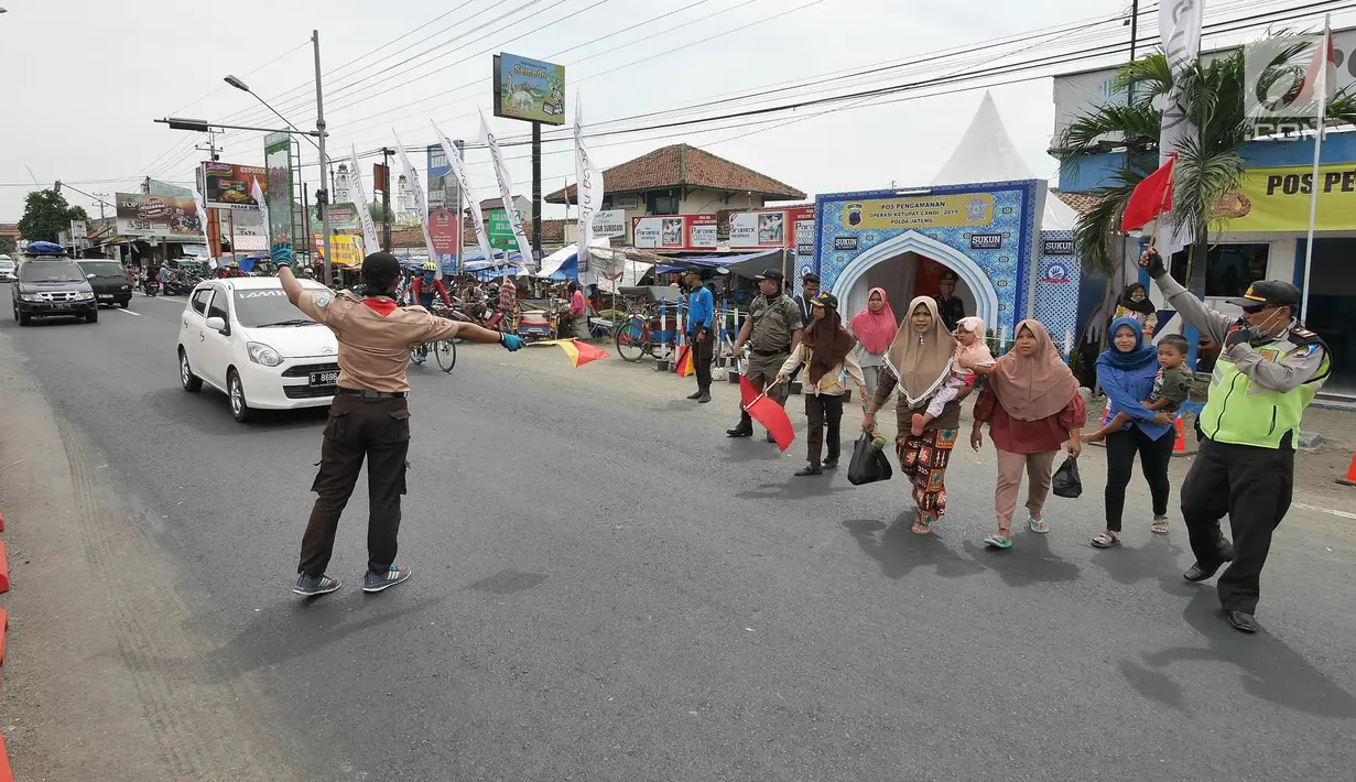 Petugas polisi dan anggota Pramuka membantu menyebrangi warga saat mengatur lalu lintas di jalur mudik kawasan pasar Surodadi, Tegal  Jawa Tengah, Senin (3/6/2019). Puluhan anggota Pramuka  membantu polisi mengatur lalu lintas selama arus mudik maupun arus balik. (Liputan6.com/Herman Zakharia)