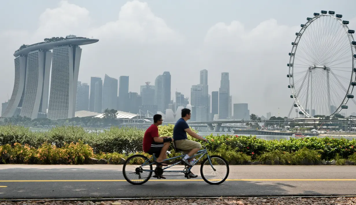 Dua orang bersepeda sambil mengamati skyline kota Singapura yang diselimuti kabut. Meskipun Singapura adalah kota dengan biaya hidup paling tinggi di dunia, namun biaya hidup di sana 10% lebih murah dibandingkan di New York. (AFP PHOTO/Roslan RAHMAN)