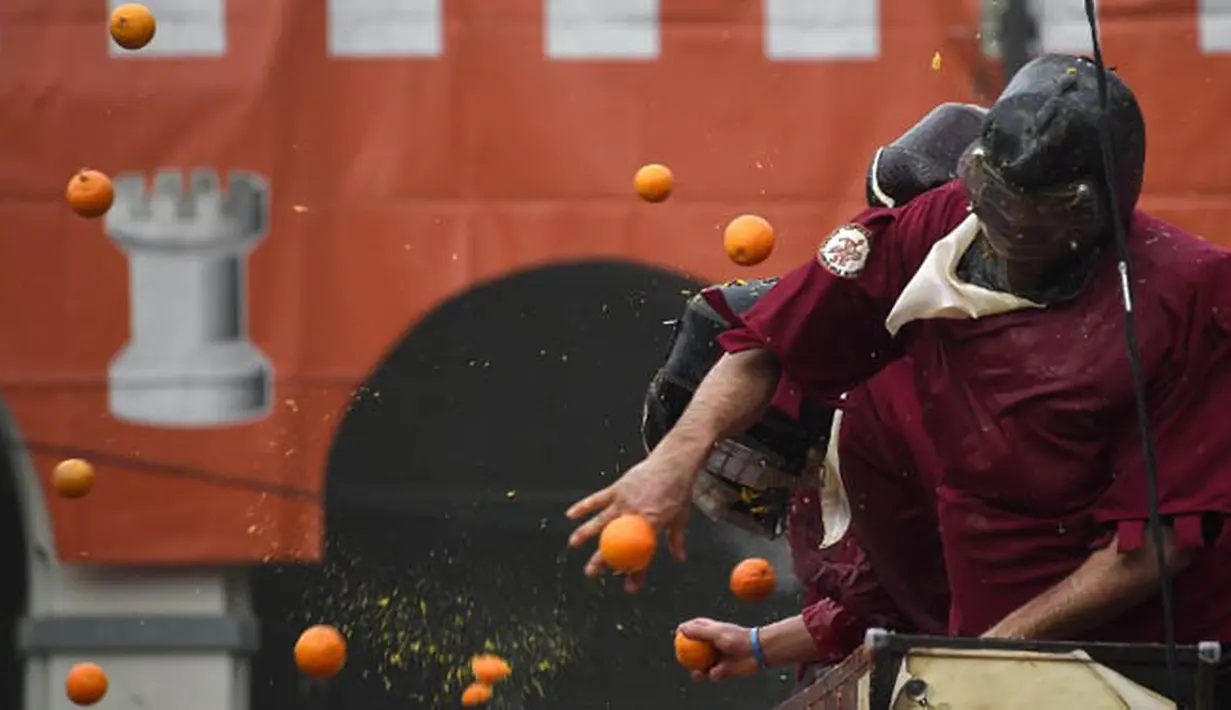 Seorang pasukan yang mengenakan helm dan kostum terkena lemparan jeruk saat perang jeruk yang diselenggarakan selama Karnaval Ivrea di Turin, Italia (16/2). (AFP PHOTO/Olivier MORIN)