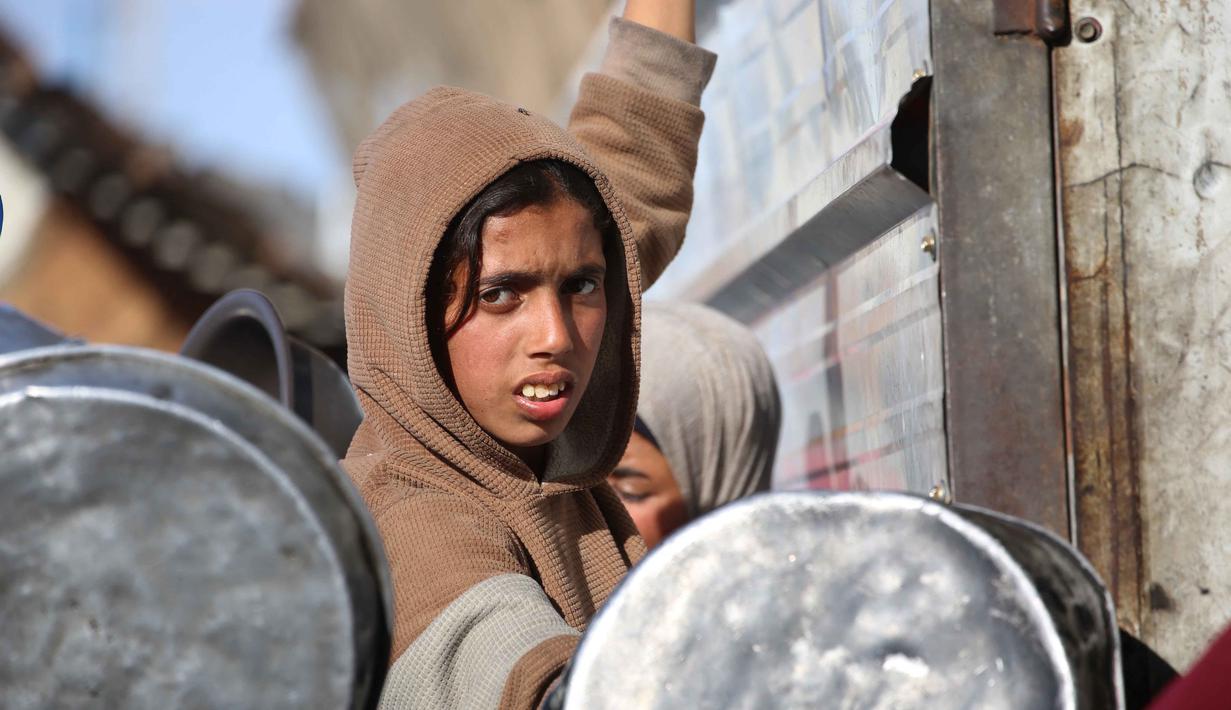 Sementara itu, mayoritas warga Gaza masih sepenuhnya bergantung pada dapur umum komunitas dan bantuan dari World Food Programme (WFP) yang menyediakan jatah tepung dan boks makanan untuk lebih dari satu juta orang. Tampak dalam foto, seorang anak pengungsi Palestina berebut untuk makanan di Khan Younis, selatan Jalur Gaza pada Jumat 6 Maret 2026. (Bashar Taleb/AFP)