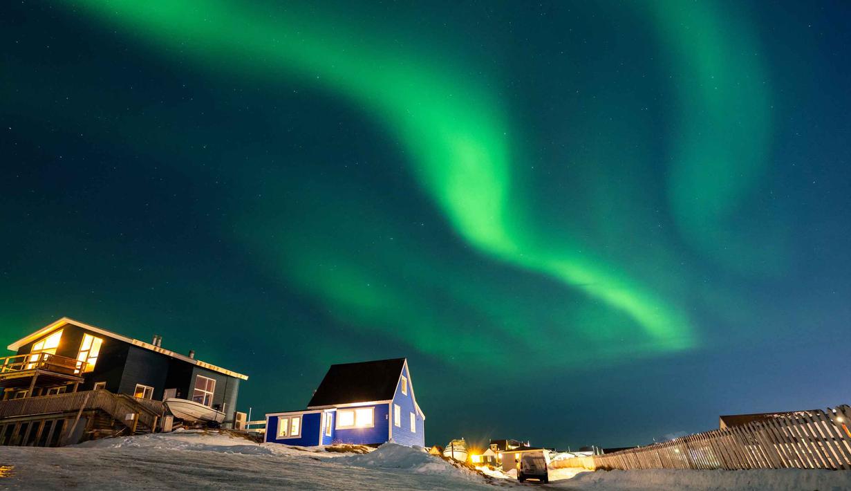 Aurora Borealis menerangi langit malam di atas rumah-rumah penduduk di Nuuk, Greenland, pada 23 Januari 2026. Cahaya hijau bersinar menghiasi langit kota Nuuk, Greenland, pada Jumat 23 Januari 2026 waktu setempat. (Jonathan NACKSTRAND/AFP)