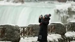Seorang turis berjaket tebal mengambil gambar di depan Air Terjun Niagara, Ontario, Kanada, Senin (9/1). Salju tebal dan angin dingin membahayakan kondisi warga. (Geoff Robins/AFP)