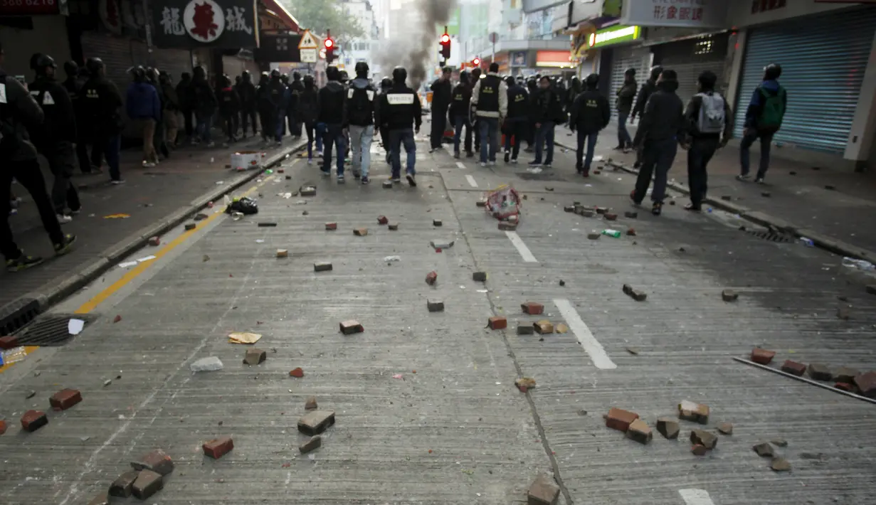 Sejumlah batu terlihat di belakang polisi anti huru hara setelah bentrokan dengan pengunjuk rasa di Mongkok, Hong Kong, Selasa (9/2). Bentrokan dimulai ketika pemerintah daerah mencoba untuk menertibkan PKL yang beroperasi. (REUTERS/Liau Chung-ren)