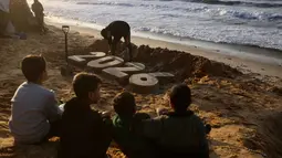 Cuaca ekstrem yang ditandai dengan hujan deras, angin kencang, dan suhu dingin memperburuk kondisi pengungsi Palestina di Gaza hingga menimbulkan angka kematian baru. Tampak dalam foto, anak-anak menyaksikan seniman Yazed Abo Jarad membuat patung pasir untuk tahun mendatang di Deir El-Balah, Jalur Gaza tengah pada 30 Desember 2025. (Bashar Taleb/AFP)
