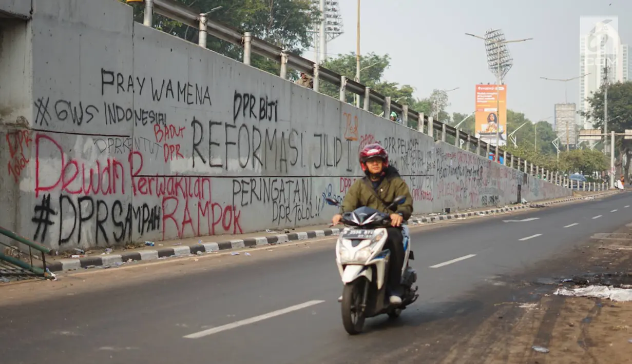 Pengendara motor melintasi coret-coretan yang menghiasi tembok di sekitar kawasan Gedung DPR, Rabu (25/9/2019). Aksi demonstrasi mahasiswa yang menolak RUU bermasalah itu berujung ricuh dan bentrok dengan polisi sehingga menyebabkan sejumlah fasilitas umum rusak. (Liputan6.com/Immanuel Antonius)