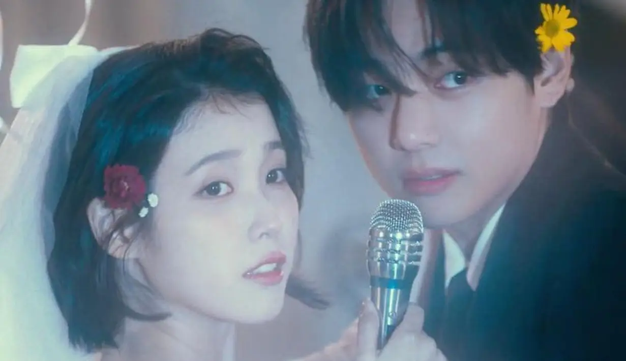 IU melengkapi penampilan dengan veil di atas rambut pendeknya. IU tampil mengaplikasikan makeup natural.  IU dan V pun kompak mengenakan bunga di salah satu kupingnya.  [YouTube/ IU Official]