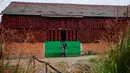 Seorang wanita berjalan melintasi rumah yang temboknya penuh dengan gantungan paprika merah untuk dikeringkan, di Desa Donja Lakosnica, Serbia, 6 Oktober 2016. Saat musim panen, warga menjemur paprika di dinding hingga atap rumah. (REUTERS/Marko Djurica)