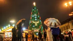 Orang-orang menyaksikan pohon Natal tradisional setinggi 45 meter di tengah hujan lebat di pasar Natal Dortmund, Jerman, Senin, 27 November 2023. (AP Photo/Martin Meissner)