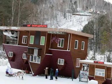 Seorang pekerja berpakaian seperti Ded Moroz atau Santa Claus dari Rusia bersama cucunya Snegurochka duduk di kereta Rusa menyambut pengunjung rumah terbalik Royev Ruchey Park, Krasnoyarsk, Rusia (7/12). (Reuters/Ilya Naymushin)