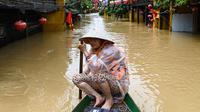 Seorang perempuan mendayung perahu di jalanan yang terendam banjir setelah hujan deras di Hoi An, Vietnam, Kamis 30 Oktober 2025. Hujan deras dengan intensitas tertinggi sepanjang sejarah memicu banjir besar di Vietnam bagian tengah. (NHAC NGUYEN/AFP)