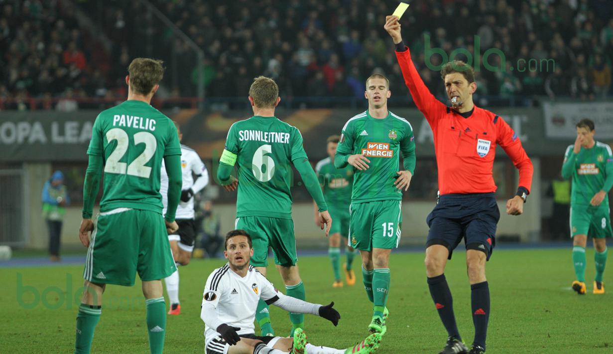 Wasit asal Italia, Paolo Tagliavento, melayangkan kartu kuning kepada pemain Rapid Vienna lantaran melanggar Pablo Piatti saat laga di Stadion Ernst Happel, Wina, Austria, Jumat (26/2/2016) dini hari WIB. (Bola.com/Reza Khomaini)