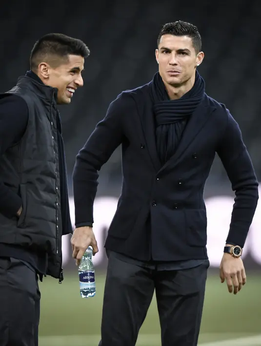 Penyerang Juventus, Cristiano Ronaldo bersama rekannya Joao Cancelo memeriksa lapangan di Stade de Suisse di Bern (11/12). Ronaldo tampil keren menggenakan setelan jas dengan syal di lehernya saat mengecek markas Young Boys. (AFP Photo/Fabrice Coffrini)