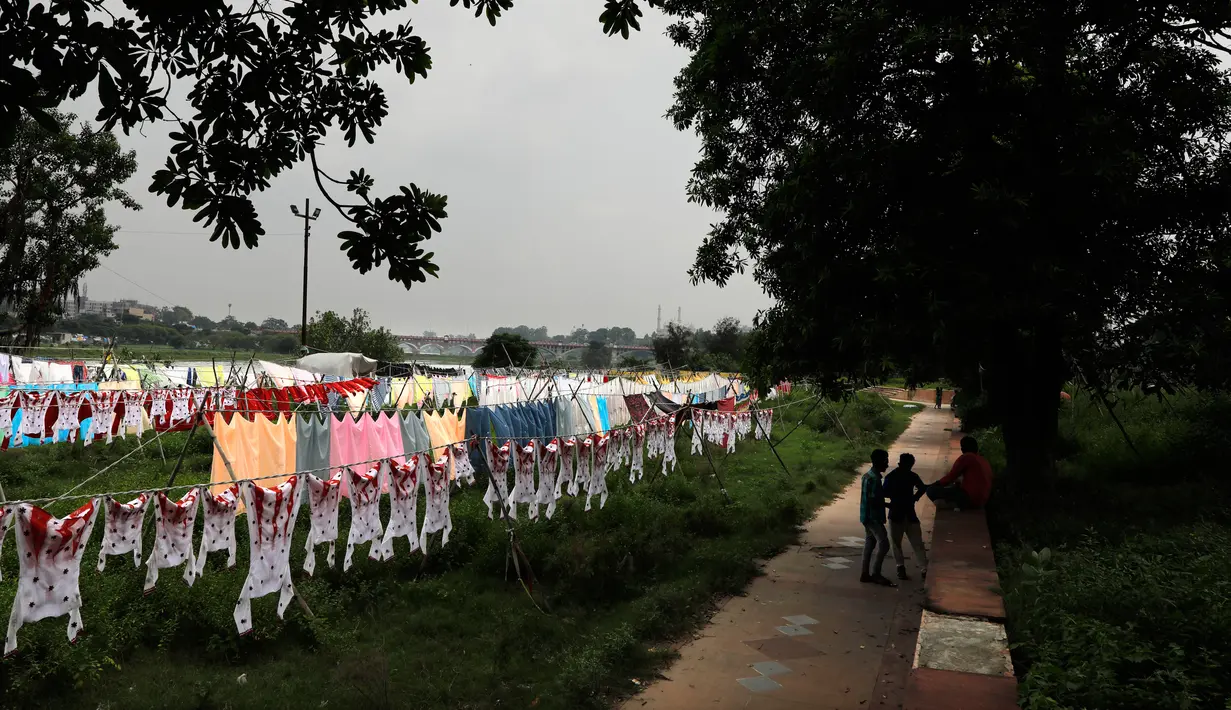 Dhobis, atau tukang cuci, menunggu pakaian yang digantung kering di antrean setelah dicuci di tepian Sungai Gomti di Lucknow, India, 12 September 2020. Dhobi adalah pekerja binatu tradisional yang mencuci pakaian dengan tangan dan menjemurnya di bawah sinar matahari. (AP Photo/Rajesh Kumar Singh)