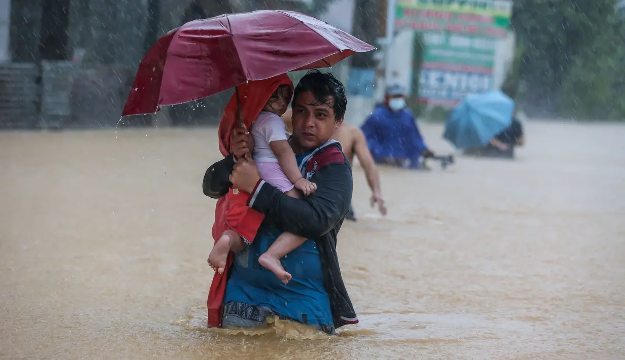 Seorang warga menggendong anaknya menembus genangan banjir yang diakibatkan oleh Topan Vamco di Provinsi Rizal, Filipina (12/11/2020). Topan Vamco membawa angin kencang dan hujan deras yang memicu tanah longsor, longsor batu, serta banjir bandang. (Xinhua/Rouelle Umali)