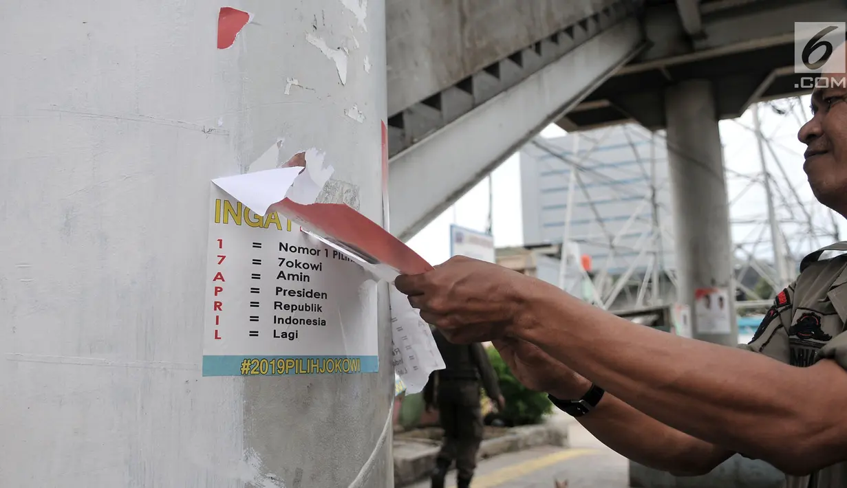 Petugas Satpol PP mencopot poster yang terpasang di JPO saat penertiban APK di sepanjang Jalan Yos Sudarso, Jakarta Utara, Rabu (13/3). APK yang dipasang di sembarang tempat dan fasilitas umum melanggar SK KPU nomor 175. (merdeka.com/Iqbal S. Nugroho)