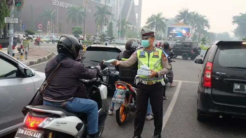 Personel Polresta Pekanbaru membagikan masker kepada pengguna jalan agar tidak menghirup kabut asap.