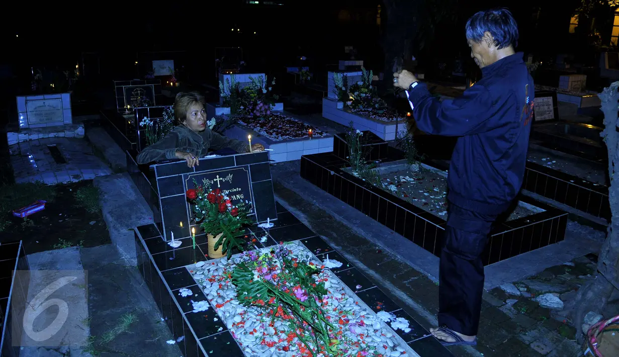 Warga mengambil gambar saat melakukan ziarah ke makam yang terdapat di sebelah Gereja Tugu, Jakarta, Kamis (24/12). Tradisi nyekar itu dilakukan usai mengikuti ibadah kebaktian malam Natal di gereja. (Liputan6.com/Gempur M Surya)