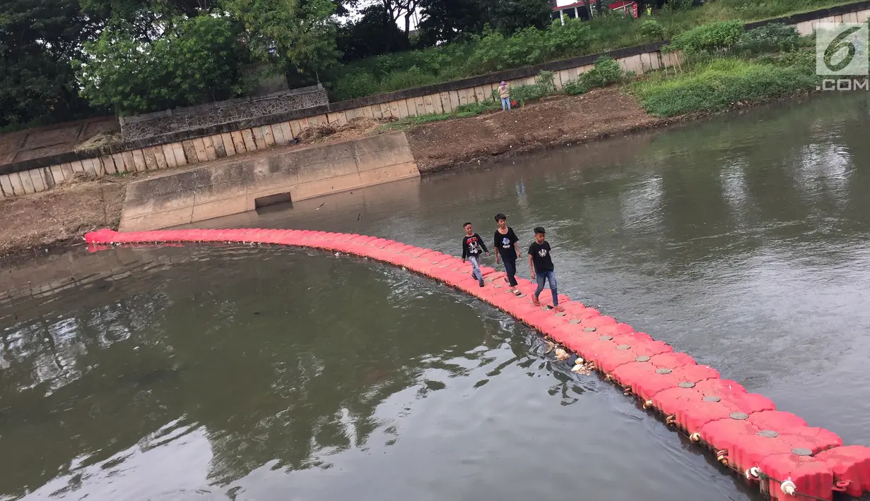 Anak-anak melintasi penyaring sampah untuk menyeberangi Kanal Banjir Timur di Jakarta, Kamis (28/12). Keberadaan penyaring sampah tersebut dimanfaatkan warga sebagai sarana menyeberang untuk mempersingkat waktu tempuh. (Liputan6.com/Immanuel Antonius)