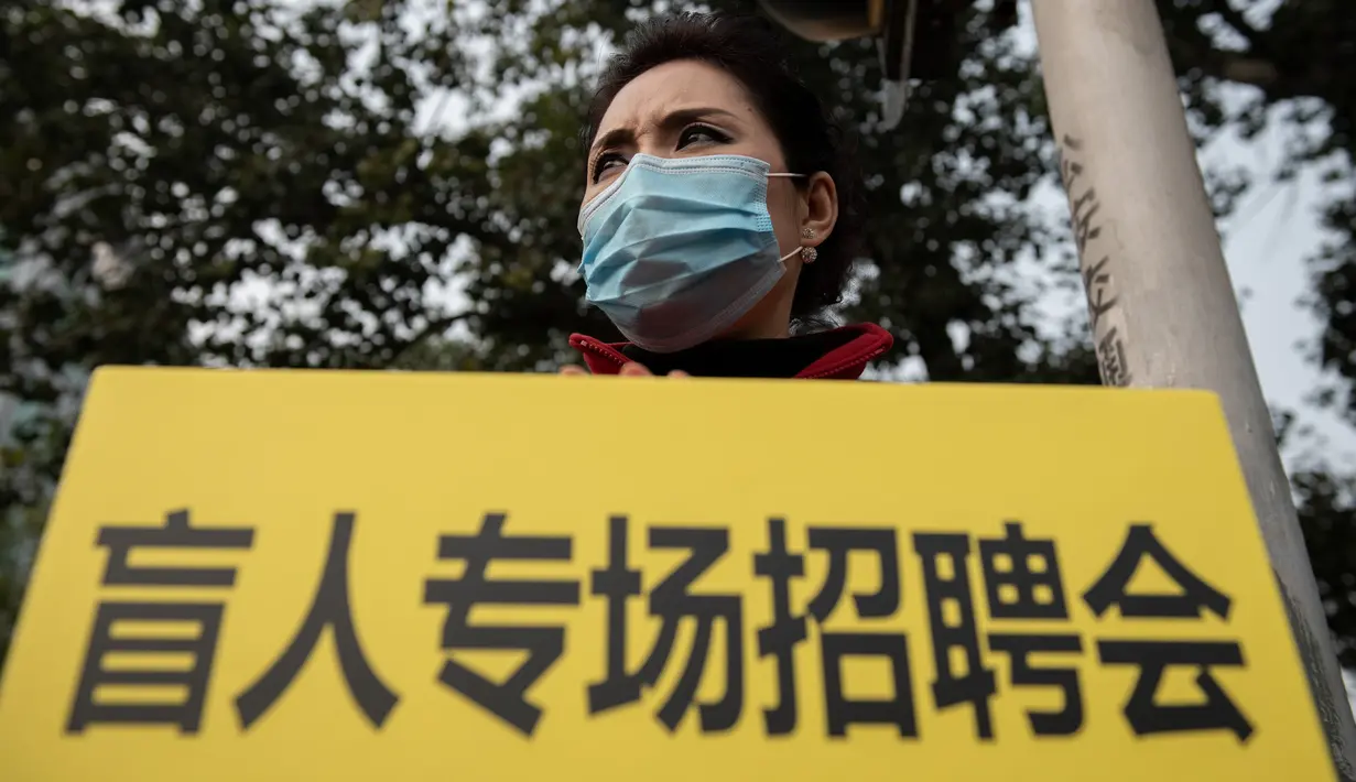 Seorang wanita memegang poster bertulisan "job fair for blind people" saat dia mengenakan masker pelindung untuk menghindari polusi udara buruk di Beijing (22/10). (AFP Photo/Nicolas Asfaouri)