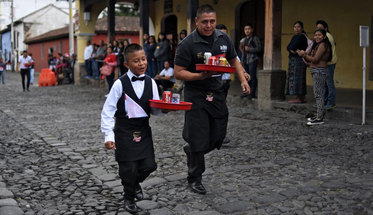 Pramusaji dan seorang anak beradu kecepatan sambil membawa nampan dalam Waiters Race ke-16 di Antigua, barat daya Ibu Kota Guatemala City, Rabu (14/11). Lomba ini diikuti oleh ratusan peserta yang merupakan pelayan restoran dan kafe. (JOHAN ORDONEZ/AFP)