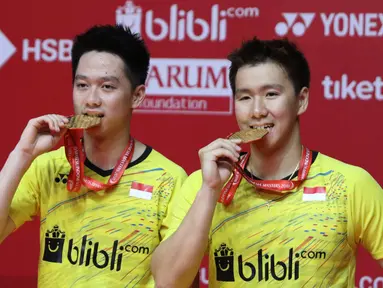 Ganda putra Indonesia Kevin Sanjaya Sukamuljo dan Marcus Fernaldi Gideon menggigit medali emas seusai mengalahkan ganda putra Cina Li Junhui dan Liu Yuchen pada babak final Indonesia Masters 2018 di Jakarta, Minggu (28/1). (Liputan6.com/Angga Yuniar)