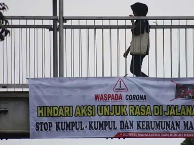 Pejalan kaki melintasi Jembatan Penyeberangan Orang (JPO) di Jalan Raya Lenteng Agung, Jakarta, Selasa (17/3/2020). Sebuah spanduk berisi ajakan menghindari kerumunan dan kumpul-kumpul untuk mencegah penyebaran virus Corona COVID-19 terpasang di JPO teresebut. (Liputan6.com/Helmi Fithriansyah)