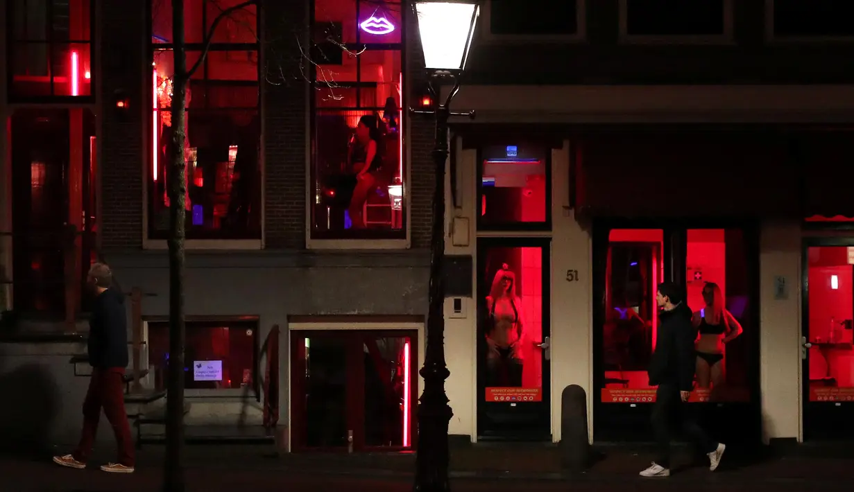 Orang-orang berjalan melewati rumah bordil di Red Light District Amsterdam, Belanda, Rabu (3/4). Red Light District merupakan kawasan prostitusi yang tersohor dan menjadi salah satu destinasi wisata di Belanda. (REUTERS/Yves Herman)