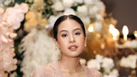 Maudy mengaplikasikan makeup natural glowing dengan lipstik coklat glossy serta blush on tipisnya. Rambutnya disanggul rapi model rambut belah tengah. [@maudyayunda]