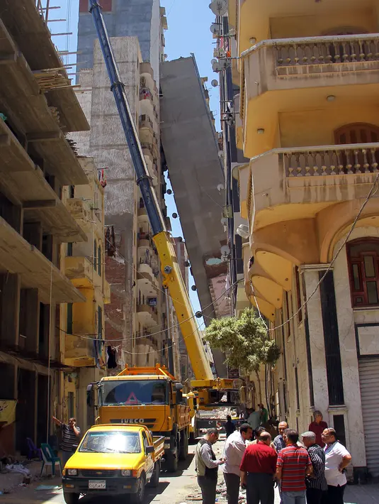 Sejumlah orang mengamati apartemen berlantai 13 yang mengalami kemiringan hingga mencapai blok apartemen lainnya di kota Alexandria, Sabtu (3/6). Pihak militer Mesir telah dipanggil untuk menghancurkan bangunan itu. (STRINGER / AFP)