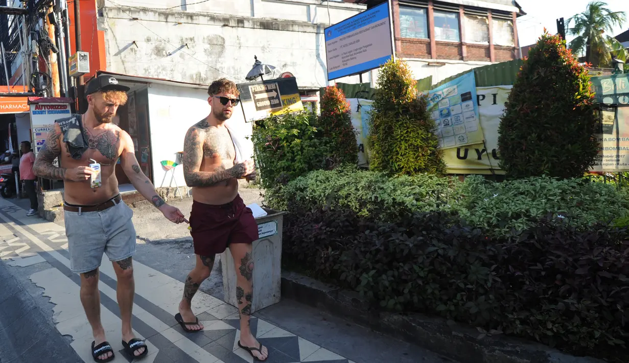 Turis mancanegara melewati papan izin mendirikan bangunan (biru) di bekas lokasi bom Bali Sari Club di Kuta, Jumat (26/4). Eks lokasi Sari Club itu bakal menjadi restoran yang menyediakan menu western dan di bangunan baru itu nantinya akan ada monumen peringatan di lantai 5. (SONNY TUMBELAKA/AFP)