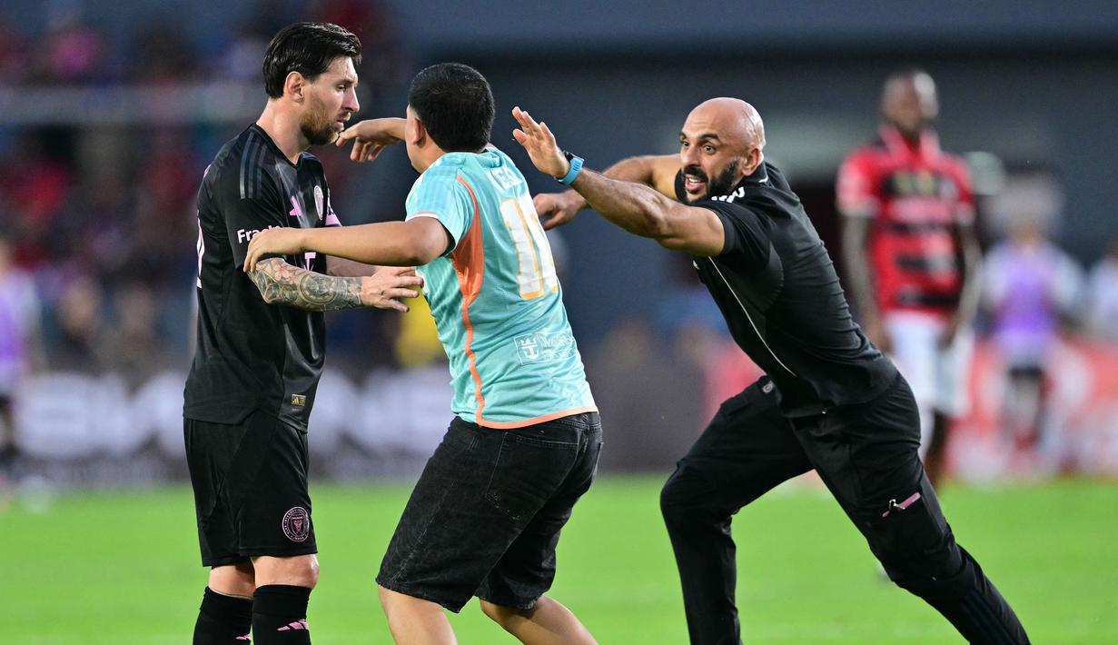 Pengawal Lionel Messi, Yassine Cheuko (kanan) berusaha menangkap seorang penyusup lapangan dalam laga persahabatan antara Inter Miami melawan Sporting San Miguelito di Stadion Romeo Fernandez, Panama, Amerika, Senin (03/02/2025) waktu setempat. (AFP/Martin Bernetti)