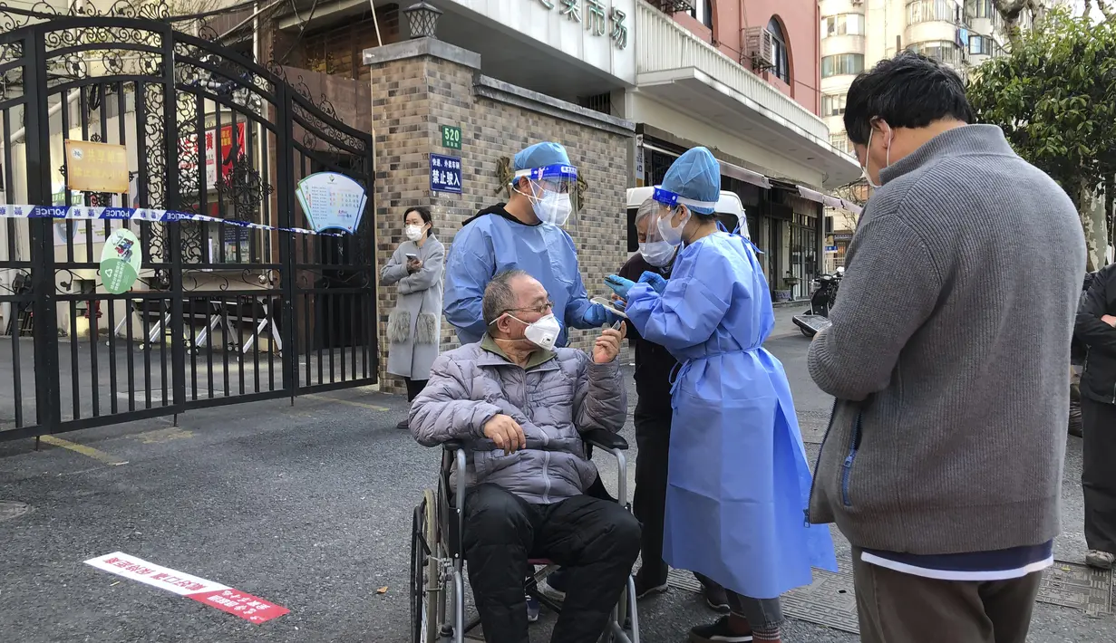 Pekerja dengan alat pelindung membantu seorang pria di kursi roda selama pengujian massal untuk penduduk di distrik Jingan, Shanghai barat (4/4/2022). China telah mengirim lebih dari 10.000 petugas kesehatan dari seluruh negeri ke Shanghai, termasuk 2.000 staf medis militer. (AP Photo/Chen Si)