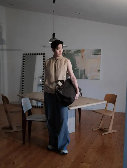 Thanapob Leeratanakachorn aktor Thailand mengenakan atasan tanpa lengan warna coklat dipadukan celana panjang abu-abu. Ia membawa Dior Normandie Tote bag hitam. [@thanapob_lee]