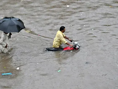 Seorang pengendara sepeda motor mendorong sepedanya melalui jalan yang banjir setelah hujan lebat di Lahore pada 5 Juli 2023. (AFP/Arif Ali)