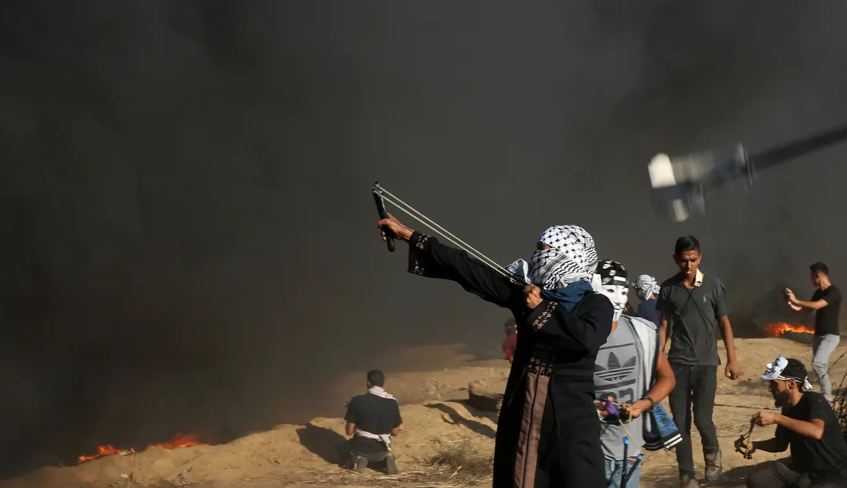 Pengunjuk rasa wanita Palestina menembakkan batu menggunakan ketapel ke arah tentara Israel saat bentrok di Khan Younis, perbatasan Gaza, Jumat (10/8). (AP Photo/Adel Hana)