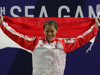 Lifter Windy Aisyah mengibarkan bendera saat naik podium usai mendapatkan medali emas SEA Games 2019 cabang angkat besi nomor 49 kg di Stadion Rizal Memorial, Manila, Minggu (1/12/2019). Windy Aisyah meraih emas dengan total angkatan 104 kg. (Bola.com/M Iqbal Ichsan)