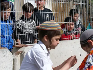 Anak-anak Palestina menyaksikan warga Yahudi merayakan Hari Purim di Jalan al-Shuhada, Kota Hebron, Tepi Barat, Kamis (1/3). Hari Purim diperingati untuk memperingati pembebasan orang-orang Yahudi dari genosida Persia kuno. (AFP PHOTO/HAZEM BADER)