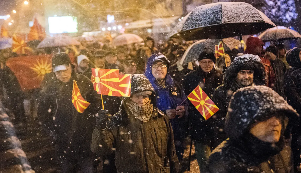 Pengunjuk rasa mengibarkan bendera Macedonia saat menggelar protes di depan gedung Parlemen, Skopje, Selasa (27/2). Di tengah hujan salju, mereka turun ke jalan memprotes wacana pengubahan nama negara mereka. (Robert ATANASOVSKI/AFP)