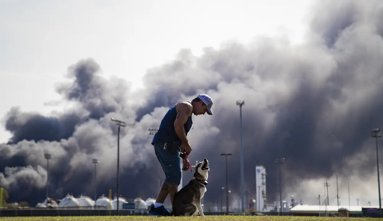 Seorang pria melatih anjingya saat asap tebal terlihat setelah ledakan di pabrik TPC Group di Port Neches, Texas (27/11/2019). Dua ledakan besar 13 jam terpisah membakar pabrik kimia dan menyebabkan tiga pekerja terluka. (Marie D. De Jesús/Houston Chronicle via AP)