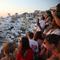 Turis menunggu matahari terbenam di desa Oia di pulau Santorini, Yunani, pada 20 Juli 2024. Seperti destinasi wisata populer lainnya, pulau Cycladic yang bertengger di atas gunung berapi itu mendekati titik jenuh, dan kini ingin membatasi jumlah kapal pesiar. (Dok: Aris Oikonomou / AFP)