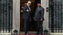 Kehadiran Larry the Cat seakan turut menyambut kunjungan Prabowo Subianto di depan pintu Downing Street. Tampak dalam foto, Larry the Cat (depan) berjalan melewati Perdana Menteri Inggris Keir Starmer (kiri) saat menyambut Presiden Indonesia Prabowo Subianto di Downing Street untuk pertemuan mereka di pusat kota London pada 20 Januari 2026. (JUSTIN TALLIS/POOL/AFP)