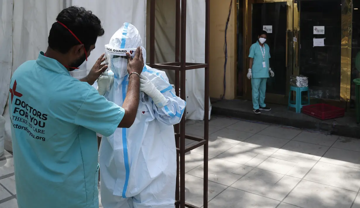 Petugas kesehatan menyesuaikan pelindung wajah rekannya yang akan masuk ke pusat karantina pasien COVID-19 di New Delhi, India, Senin (19/4/2021). New Delhi memberlakukan lockdown selama seminggu untuk mencegah runtuhnya sistem kesehatan di tengah ledakan kasus COVID-19. (AP Photo/Manish Swarup)
