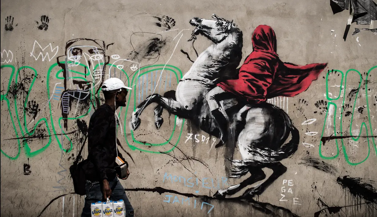 Seorang pria berjalan melewati mural yang diduga karya seniman sekaligus aktivis Banksy di Paris, Prancis, Minggu (24/6). Banksy menyoroti kebijakan pemerintah yang menomorduakan pencari suaka di Eropa. (PHILIPPE LOPEZ/AFP)