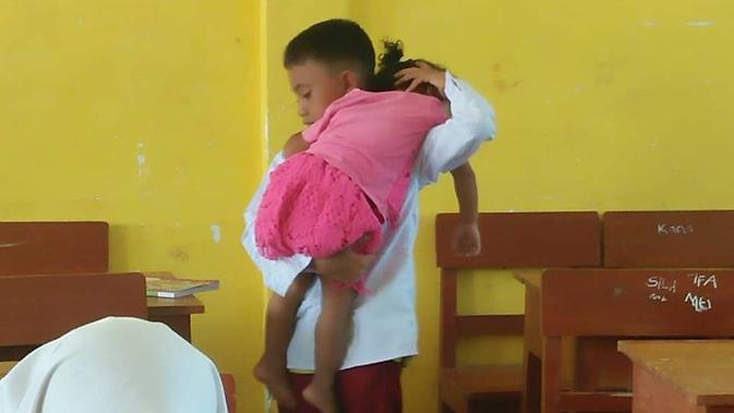 (Foto: Leendya Putry Kurniawati/Facebook) Seorang siswa SD di Sampang, Madura membawa adiknya ke sekolah sambil menuntut ilmu.