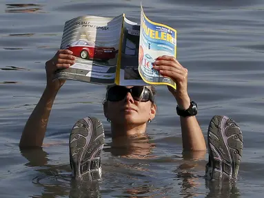 Seorang wisatawan wanita berendam sambil membaca majalah di Danau Tus, Khakassia, barat daya dari kota Siberia Krasnoyarsk, Rusia (18/7/2015). Selama musim panas, warga Rusia dari berbagai daerah melakukan perjalanan ke danau Tus. (REUTERS/Ilya Naymushin)