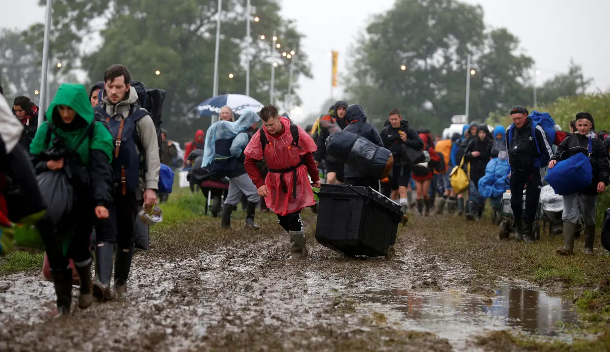 Penonton Festival Glastonbury tampak melewati jalanan yang banjir dan berlumpur saat tiba di Worthy Farm, Somerset, Inggris, (22/6). Festival Glastonbury merupakan festival musik paling populer di dunia. (REUTERS / Stoyan  Nenov)