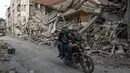 <p>Warga mengendarai sepeda motor di jalan di sebelah puing-puing bangunan yang runtuh di Hatay pada 6 Maret 2023, satu bulan setelah gempa besar melanda Turki tenggara. Gempa bumi besar berkekuatan magnitudo 7,8 mengguncang sebagian besar Turki dan sebagian Suriah pada 6 Februari 2023, menewaskan lebih dari 50.000 orang di kedua negara, dengan sekitar 46.000 di pihak Turki. (OZAN KOSE / AFP)</p>
