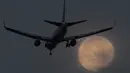 Sebuah pesawat bersiap mendarat di bandara Heathrow saat fajar dengan latar belakang Supermoon di London, Inggris, Senin (17/10). Fenomena bulan purnama terlihat lebih besar dan terang karena berada di jarak terdekat dengan bumi. (Reuters/Toby Melville)