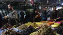 Sejumlah kios berjejer rapi, menawarkan beragam kebutuhan seperti acar, kurma, dan rempah-rempah yang menjadi incaran para pembeli. Tampak dalam foto, seorang wanita Palestina berdiri di depan sebuah toko yang menjual zaitun di pasar Zawiya, Kota Gaza, pada Rabu 18 Februari 2026. (Omar AL-QATTAA/AFP)