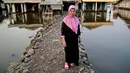 Kumaison berdiri di jalan setapak menuju rumahnya di lingkungan banjir di Timbulsloko, Jawa Tengah, Indonesia, 30 Juli 2022. Kumaison mengatakan rumahnya telah ditinggikan dengan beton dan tanah sampai tiga kali karena banjir yang lebih tinggi. (AP Photo/Dita Alangkara)
